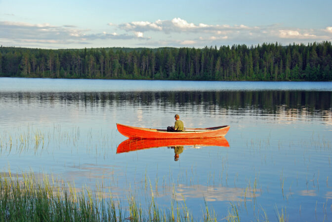 Man sitting in a red canoe on a lake in Finland and fishing at s