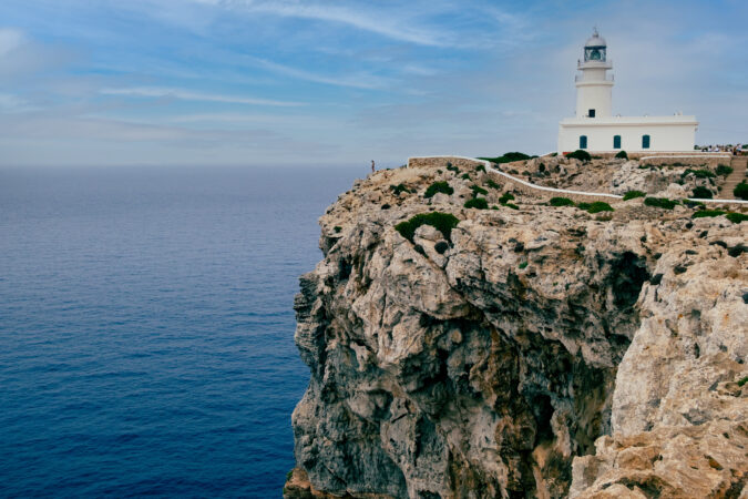 Menorca, Spain View of Cavalleria lighthouse with rocky cliff during a summer day with dramatic cloudy sunset in the balearic island of Menorca in Spain