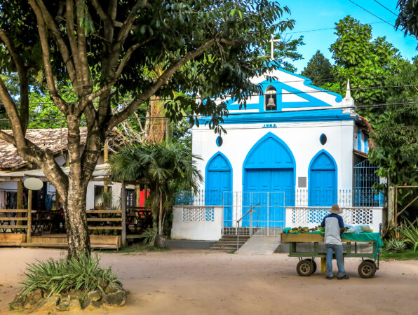 Small blue and white chapel, with a fruit seller and a large tree in front, Barra Grande, Bahia, Brazil