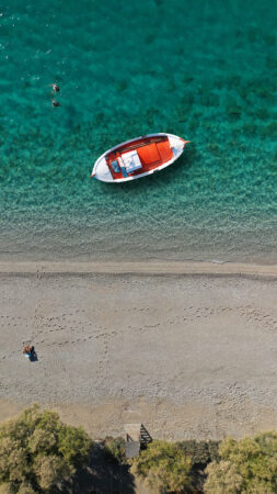 Aerial drone top down photo of traditional red wooden boat in turquoise clear beach of Ganema in island of Serifos, Cyclades, Greece